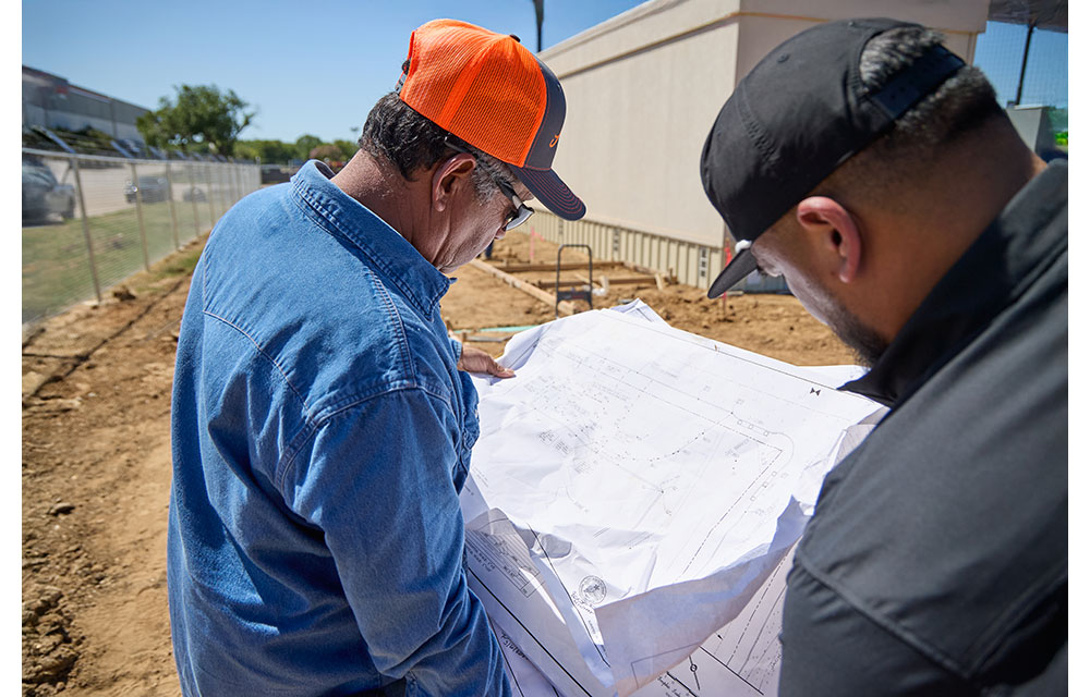 Two men, Benny and Leno Aguilar, review a large set of construction blueprints.